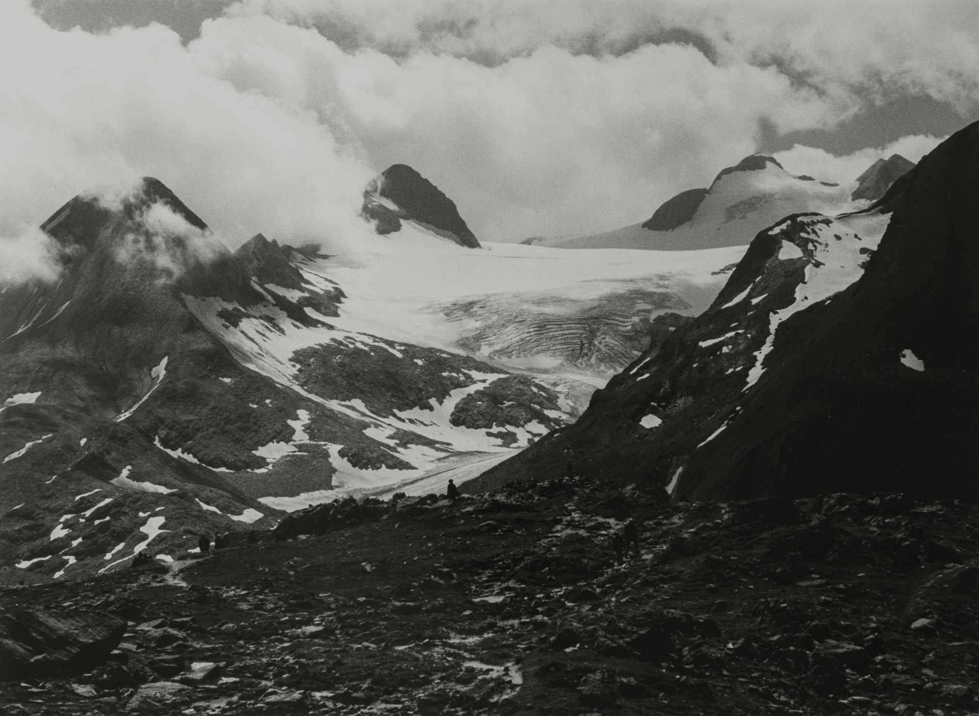 Schwarzweiß-Fotografie verschneiter Gebirgslandschaft. Die Wolken berühren die Gipfel