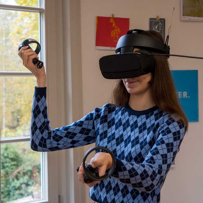 Eine Besucherin mit VR-Brille und Joysticks in den Händen.