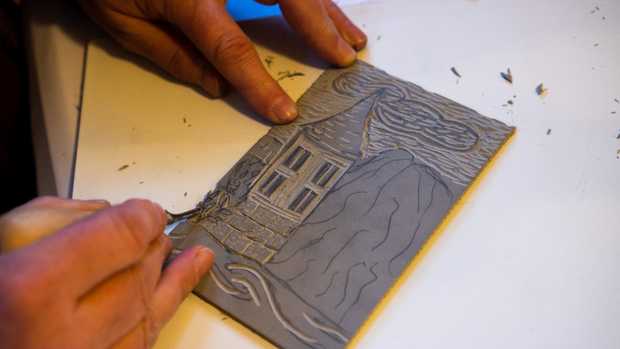 Eine Linolplatte mit einem Motiv vom Hölderlinturm. Jemand schnitzt aus einer Linolplatte die Linien einer Pflanze heraus.